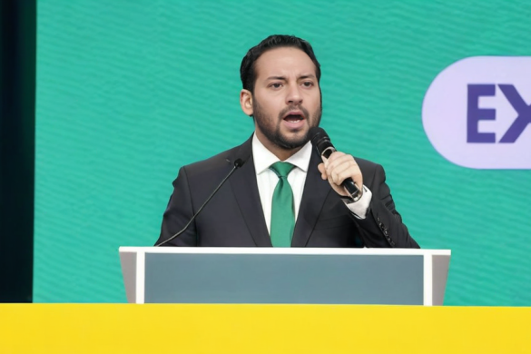 un hombre con traje y corbata hablando en un podio con un micrófono frente a él y un ex logo detrás de él, Federico Uribe, Ignacio Fernández Ríos, un holograma, tachismo