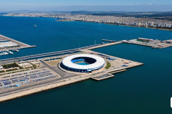 un gran edifici assegut al damunt d'un moll al costat d'una massa d'aigua amb un pont al fons, Almada Negreiros, vista aèria, una fotografia microscòpica, land art