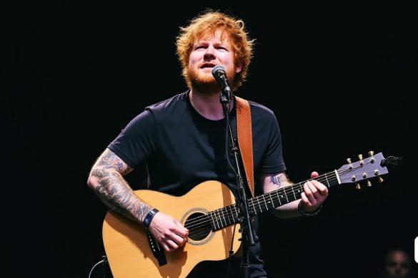 un home amb barba i tatuatges tocant una guitarra a l'escenari amb un micròfon a la mà i un micròfon a l'altra mà, Ed Benedict, tatuatges, una foto a color, premsa privada
