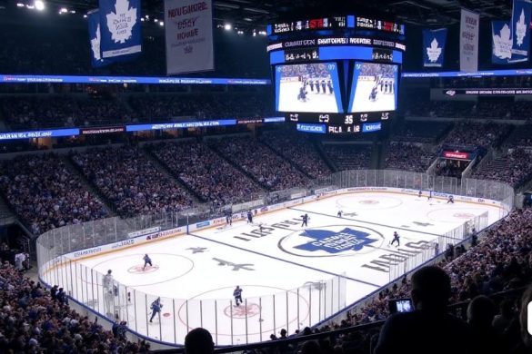 La escena en Scotiabank Arena es eléctrica pero sombría, llena de un mar de camisetas 'azul y blanca', los colores de los Toronto Maple Leafs. Los fanáticos, una mezcla de niños esperanzados y adultos cansados, están sentados con anticipación, sus caras que reflejan una mezcla de emoción y ansiedad. La arena está adornada con grandes pancartas de 'Maple Leafs' que cuelgan de las vigas, mientras que el hielo debajo brilla bajo las brillantes luces de la arena, que muestra el icónico logotipo de 'hoja de arce' en el hielo central. En primer plano, Mitch Marner, un extremo de '28 años ', es capturado a mitad de acción, su expresión una mezcla de determinación y frustración mientras intenta navegar por un defensor. La tensión es palpable a medida que el marcador se cierne en el fondo, mostrando el puntaje de '6-1', un marcado recordatorio del resultado del juego. El estado de ánimo de la multitud cambia dramáticamente, con algunos fanáticos visiblemente molestos, mientras que otros se ven dejando sus asientos, al